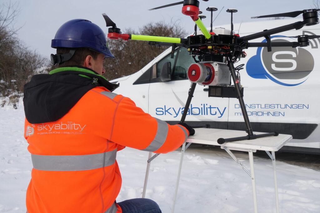 Arbeiter mit Warnweste und Helm arbeitet am RIEGL-Rotlichtscanner einer Drohne